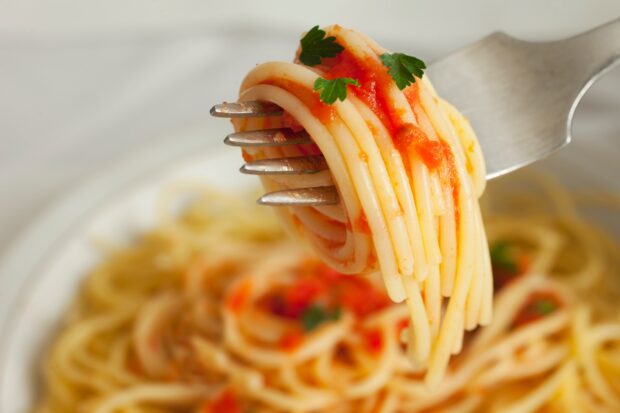 A close up of pasta with tomato sauce and parsley on a fork