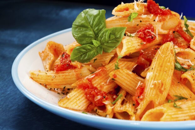 Penne pasta with tomato sauce and basil leaves on a white plate