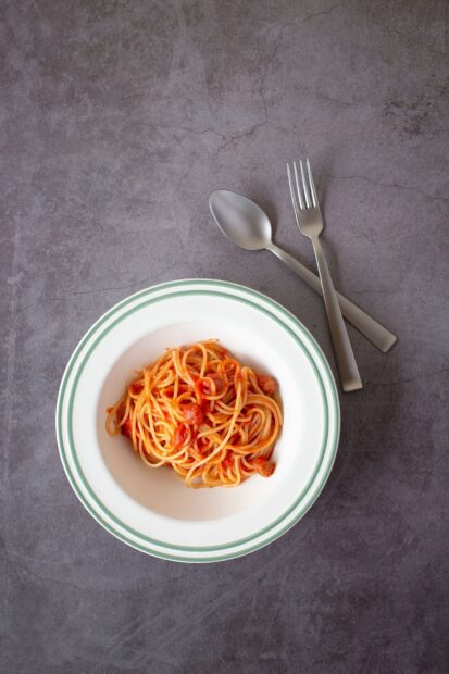 A delicious pasta dish with tomato sauce served in a white bowl on a textured surface