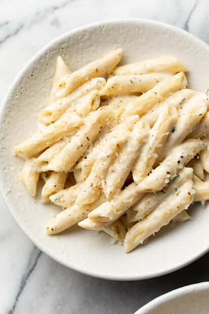 Creamy penne pasta with herbs and black pepper on a white plate