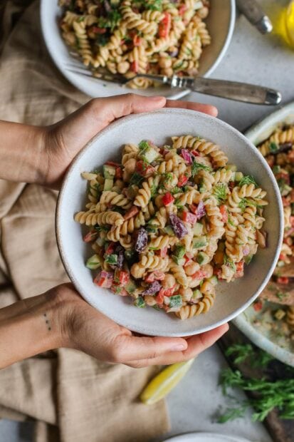 A bowl of pasta salad with chickpeas and fresh vegetables held by hands
