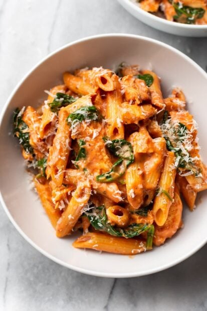 Creamy penne pasta with spinach and grated cheese in a white bowl
