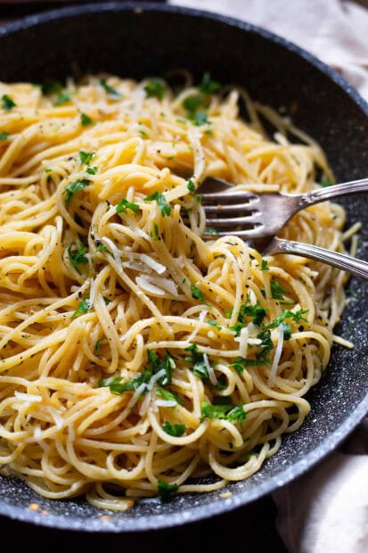 Delicious pasta tossed with herbs and grated cheese in a black pan with forks