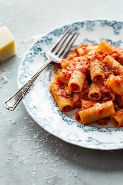 Rigatoni pasta with tomato sauce on a decorative plate with grated cheese scattered on the table