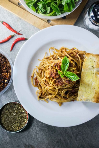 Spaghetti pasta with meat sauce and basil served with garlic bread on a white plate