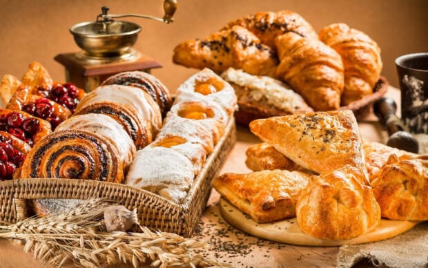 A variety of fresh pastry arranged in baskets and plates with wheat grains and a vintage coffee grinder in the background