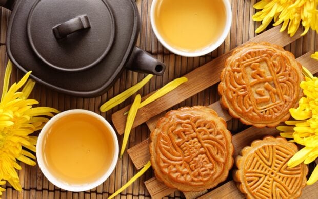 Traditional pastry with Chinese characters served with tea and yellow flowers on bamboo mat