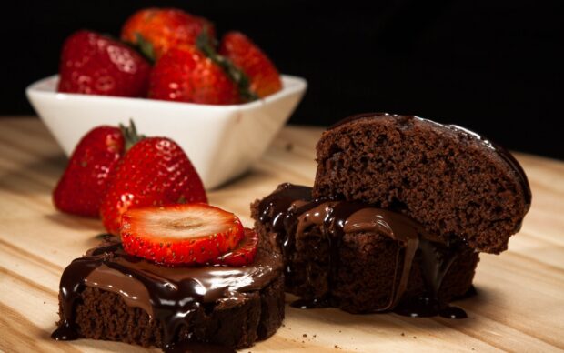 Chocolate pastry with melted chocolate and fresh strawberries on wooden surface