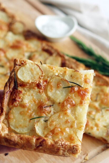 A freshly baked potato pastry topped with melted cheese and rosemary leaves