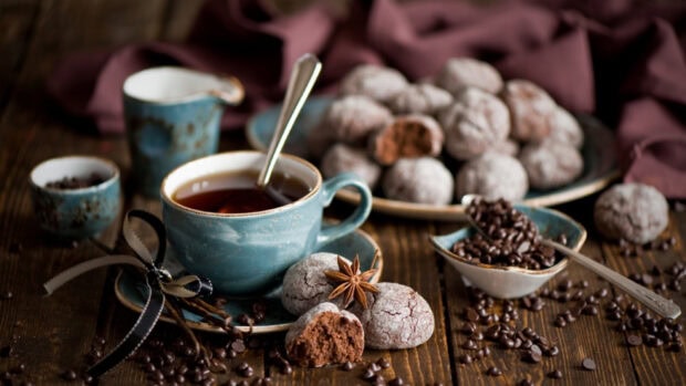 A cup of tea with cracked chocolate pastries and coffee beans on a wooden table