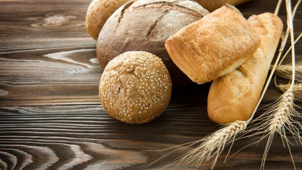 Various fresh pastry including sesame bun and crusty bread on wooden table