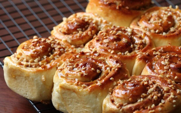 Freshly baked cinnamon rolls topped with chopped nuts on a cooling rack