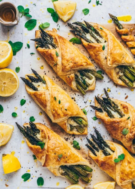Golden baked pastry with fresh asparagus and herbs on a white surface