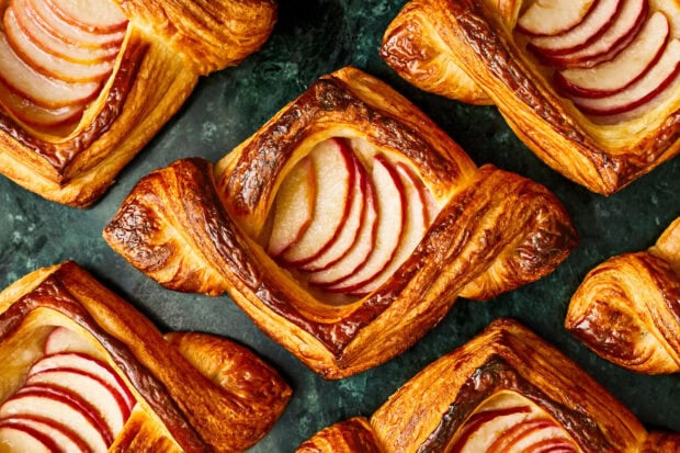 Delicious pastry with sliced apples on flaky golden crust displayed on dark surface