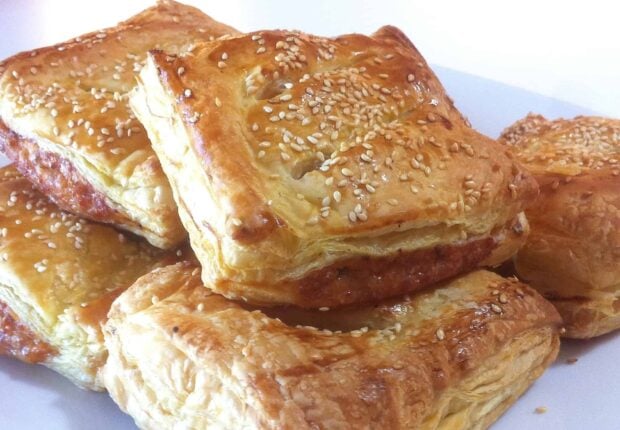 Golden pastry filled with meat and topped with sesame seeds on a white plate