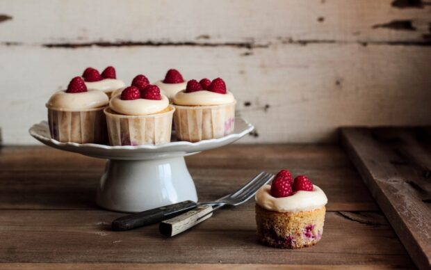 A close up of cupcakes topped with cream and raspberries on a wooden table