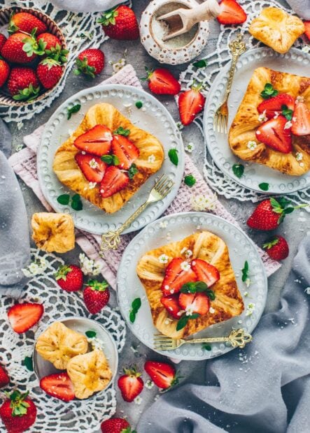 Delicious pastry topped with fresh strawberries and mint leaves on plates surrounded by scattered strawberries and flowers