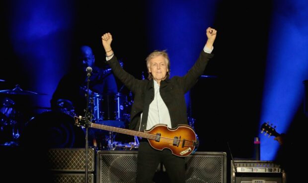 Paul Mccartney performing with raised hands on stage at a concert