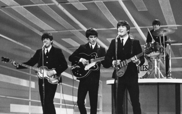Paul Mccartney playing guitar on stage with the Beatles band members performing live