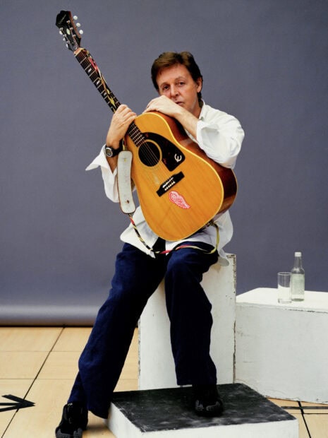 Paul Mccartney sitting and holding an acoustic guitar in a casual pose