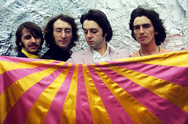 Paul Mccartney and band members holding a colorful striped fabric in front of a silver background