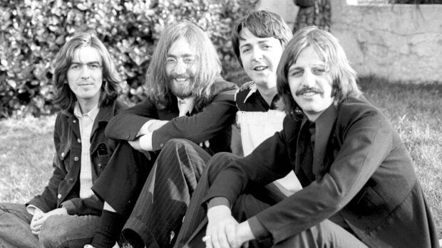 Paul Mccartney sitting with band members in a relaxed outdoor setting