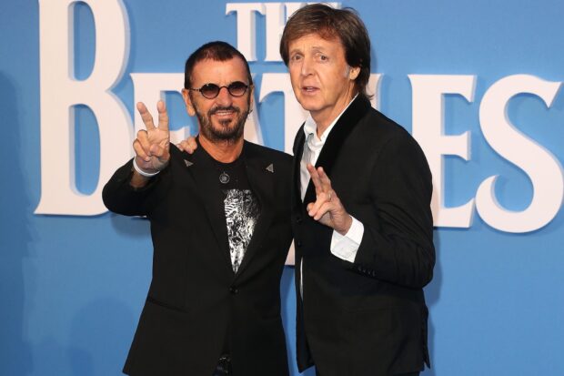 Paul Mccartney standing next to a man making peace signs in front of a Beatles poster