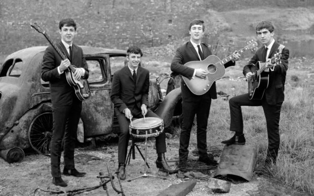 Paul Mccartney and band members playing instruments outdoors with a vintage car in the background