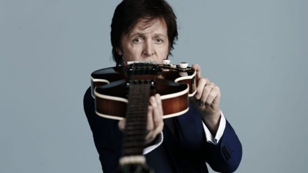 Paul Mccartney holding a guitar pointing towards the camera with a focused expression