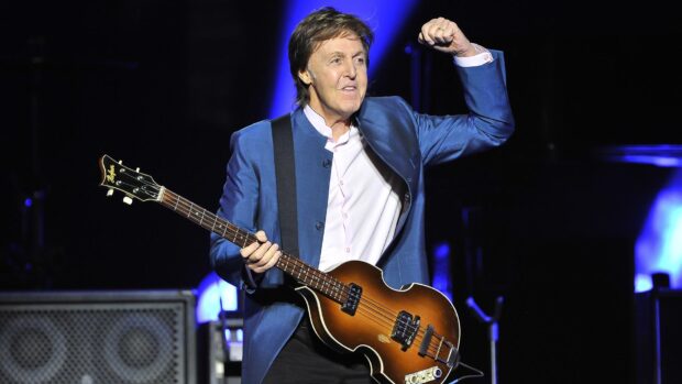Paul Mccartney performing on stage with his guitar in a blue jacket