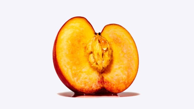Fresh peach fruit half showing the seed and juicy texture on a white surface