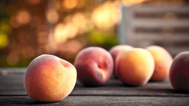 Fresh peach resting on wooden surface with blurred peaches in the background