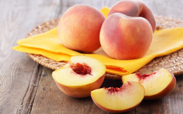 Fresh peach halves and slices placed on a wooden surface with whole peaches in the background