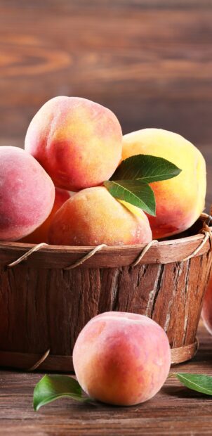 Fresh ripe peach with green leaves in a wooden basket on a rustic table