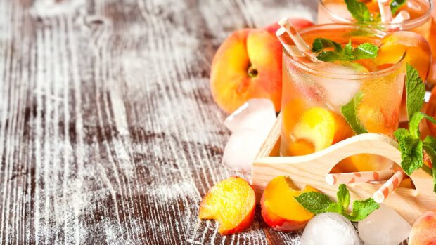 Fresh peach slices with mint leaves and ice cubes on a wooden table