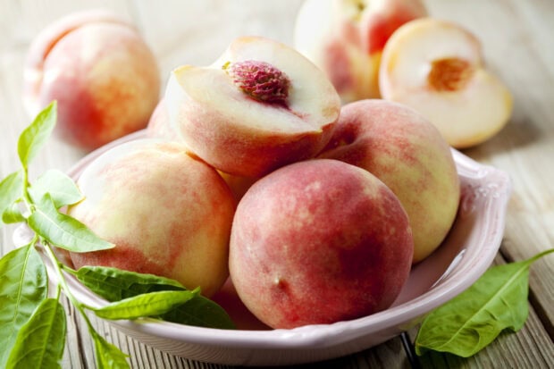 Fresh ripe peach close up with green leaves in a bowl on wooden table