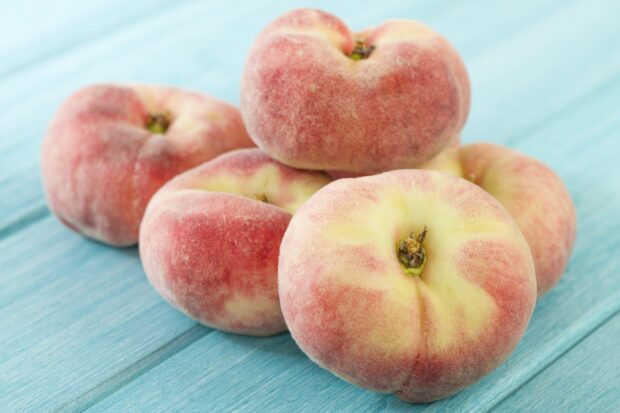 Fresh flat peaches resting on a blue wooden surface showing natural colors and texture