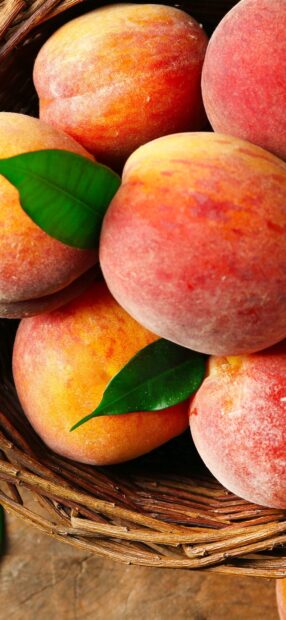 Fresh ripe peaches with green leaves in a rustic basket