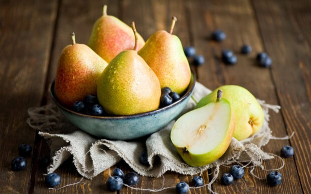 Fresh pears in a bowl with fresh blueberries on a wooden table with a fabric napkin