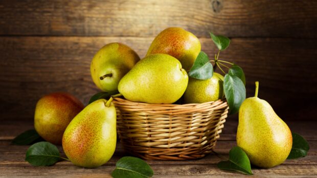 Fresh ripe pear with green leaves in a woven basket on a wooden table