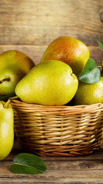 Fresh pear fruit in a woven basket with green leaves on wooden surface