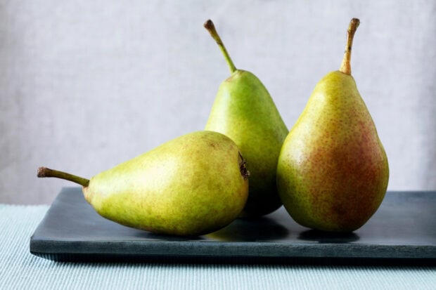 Three fresh green pears placed on a black tray with a soft background