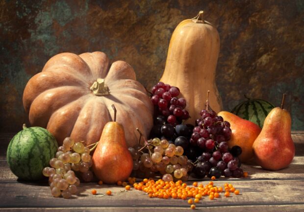 A fresh pear surrounded by various fruits on a wooden table