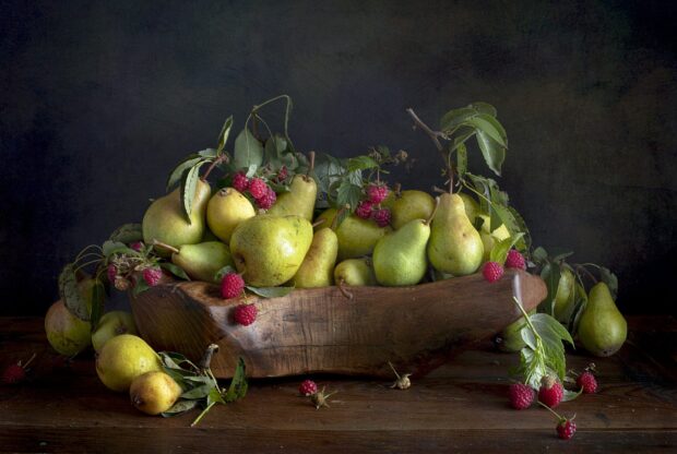 A wooden bowl filled with fresh pears and raspberries on a rustic wooden table