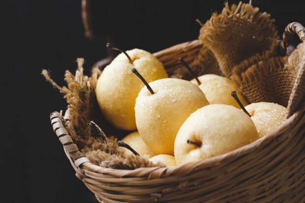 A basket filled with fresh pears covered in water droplets on a dark background