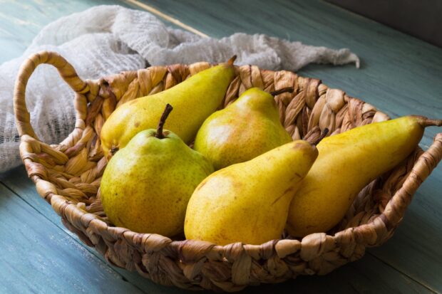 Fresh ripe pears placed in a woven basket on a blue wooden surface