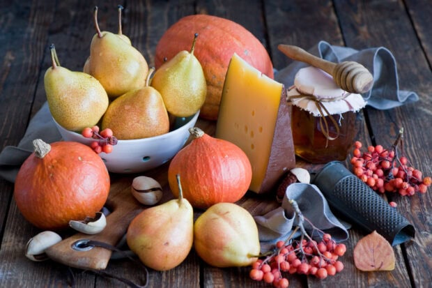A bowl of ripe pears arranged with pumpkins and cheese on a wooden table