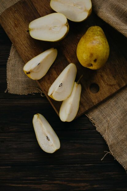 Fresh pear slices placed on a wooden board with a whole pear beside them