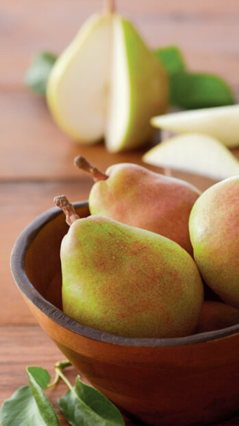 Fresh green pear fruit in a wooden bowl with leaves on a table