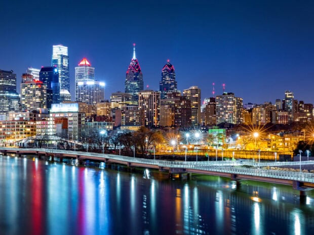 Nighttime cityscape of Pennsylvania skyline with illuminated buildings and river reflections